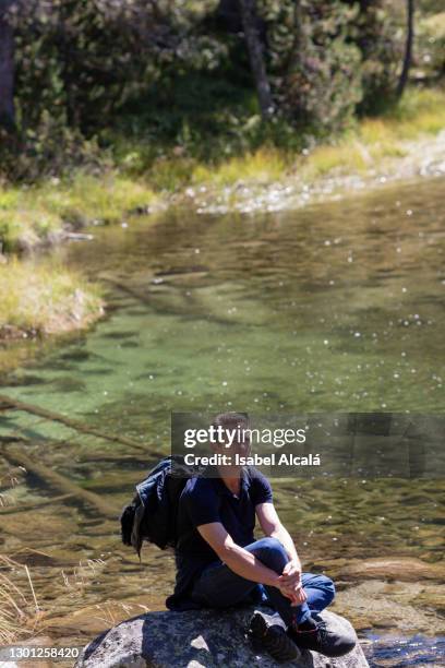 hiker mature man resting on a rock on the river. copy space - valle de arán fotografías e imágenes de stock