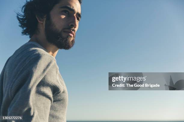 handsome man looking away against clear blue sky on sunny day - clear sky stockfoto's en -beelden