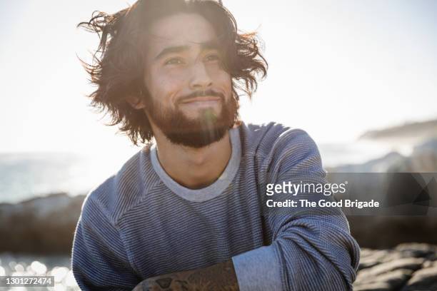 portrait of young man at beach on windy day - beschaulichkeit stock-fotos und bilder