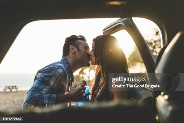 young couple kissing by car at beach - pecking stock pictures, royalty-free photos & images