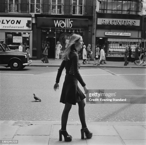 Gale Phillips wearing platform shoes on a shopping street in the UK, 3rd May 1973. In the background are Wallis and Ratners stores.