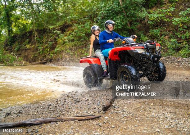 コスタリカの4x4バイクで小さな小川を渡るお父さんと娘 - quadbike ストックフォトと画像