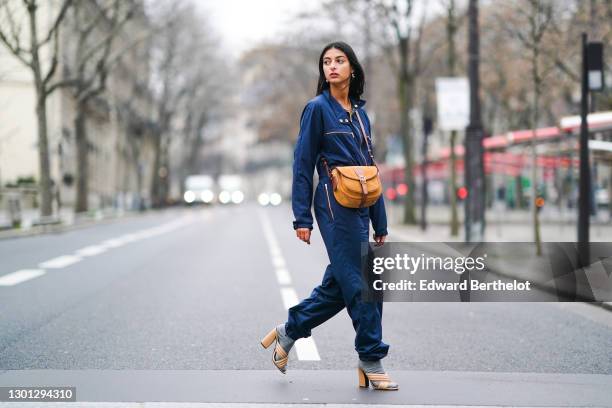 Melanie Darmon wears pearl earrings, a blue jumpsuit, a brown suede bag with leather parts from Gérard Darel, gray wool socks, beige leather high...