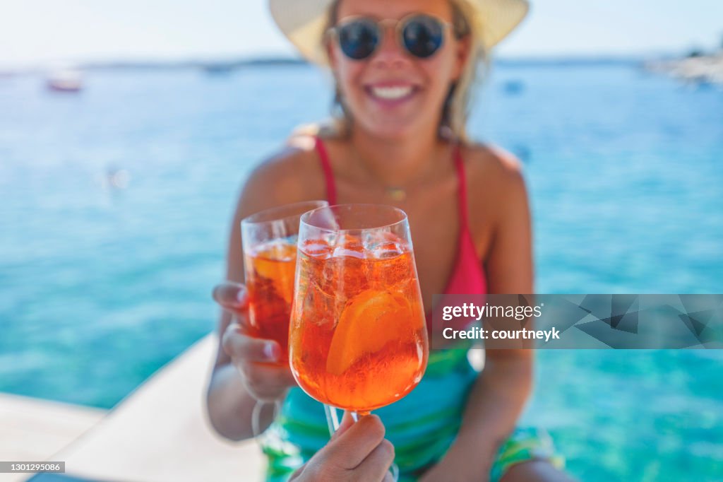 Paar dat met een spritzcocktail op een dek naast de oceaan roostert.