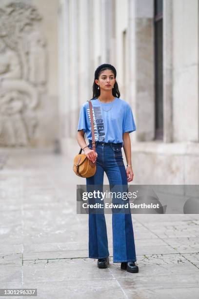 Melanie Darmon wears a golden necklace, pearl earrings, a headband from Maison Margiela, a golden bracelet, a blue t-shirt from Margiela, a brown...