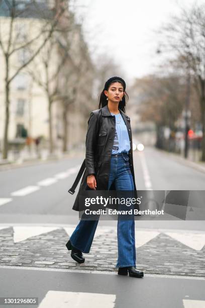 Melanie Darmon wears pearl earrings, a headband from Maison Margiela, a black leather long coat from Gerard Darel, a golden necklace, a blue t-shirt...