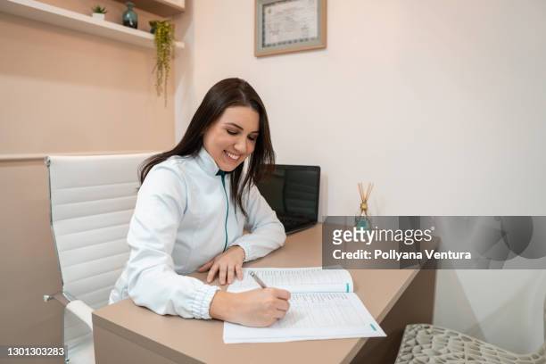happy doctor woman filling prescription - reference book stock pictures, royalty-free photos & images