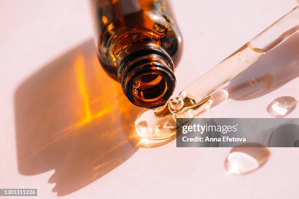 drops of facial serum or polyglutamic acid pouring out of amber glass bottle nearby pipette on pink background. trendy products of the year. health and wellness concept - etherische olie stockfoto's en -beelden