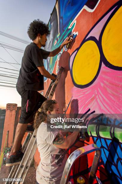 young man and woman creating graffiti on an outside wall. street art. - street artist - fotografias e filmes do acervo