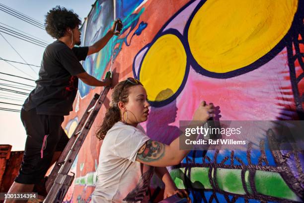 young man and woman creating graffiti on an outside wall. street art. - street artist - fotografias e filmes do acervo