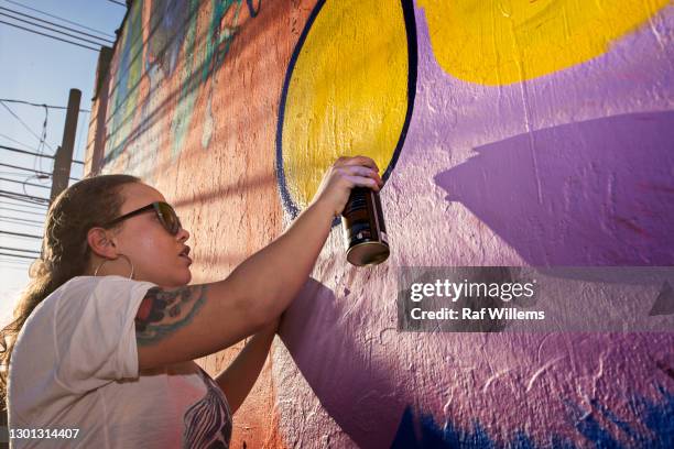 woman with a spray can, creating graffiti on an outside wall. - street artist - fotografias e filmes do acervo