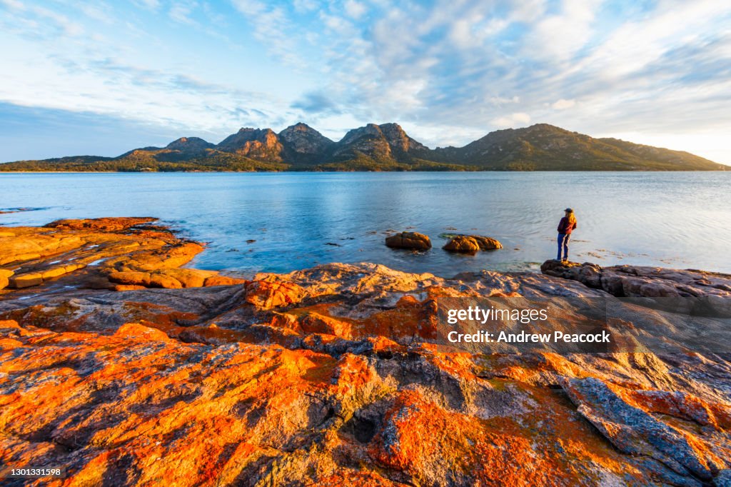 A woman enjoys a sunset view of The Hazards from Coles Bay