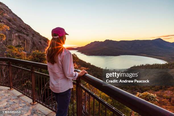 a woman watches sunrise at wineglass bay lookout, freycinet national park - tasmania landscape stock pictures, royalty-free photos & images