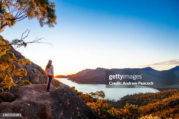 a woman watches sunrise at wineglass bay lookout, freycinet national park - australian landscapes stock pictures, royalty-free photos & images