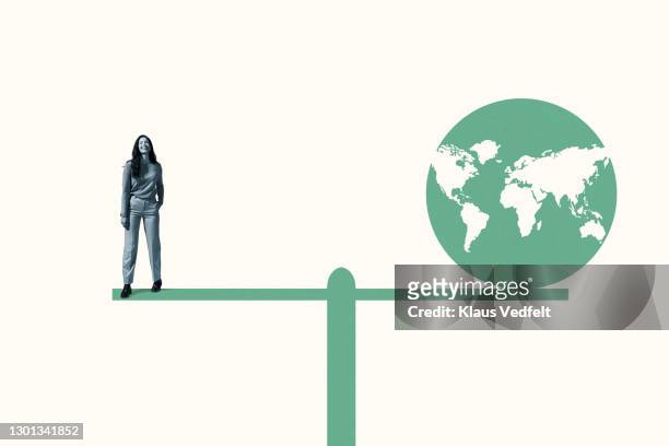 woman standing with green planet earth on seesaw - responsibility stock-fotos und bilder