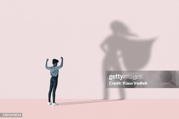 woman flexing muscles in front of superhero shadow - femme de pouvoir photos et images de collection