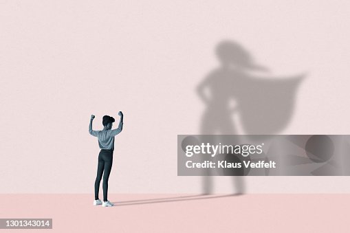 Woman flexing muscles in front of superhero shadow Woman flexing muscles in front of superhero shadow