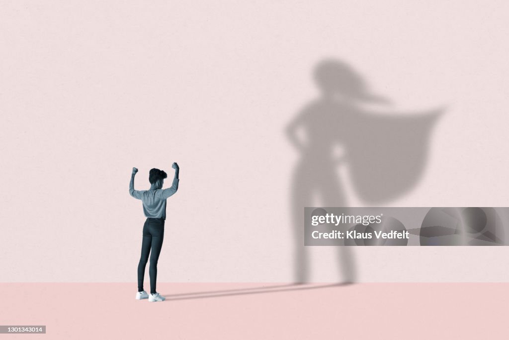Woman flexing muscles in front of superhero shadow