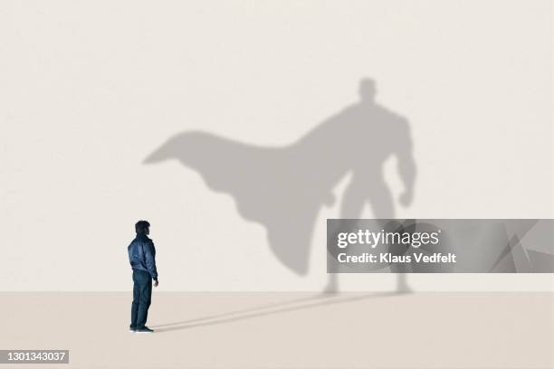 young man standing in front of superhero shadow - longue ombre ombre photos et images de collection