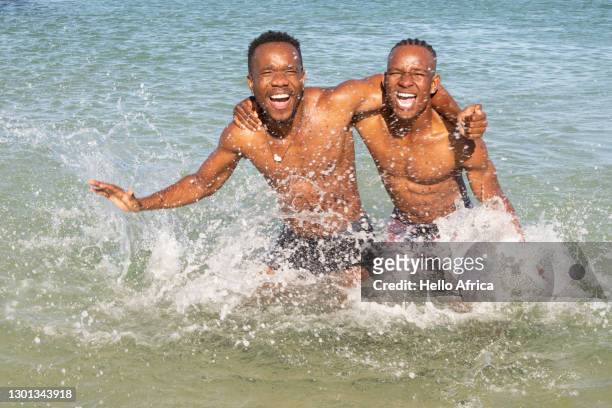 two young men messing around in the ocean. - hunky guy on beach stock pictures, royalty-free photos & images