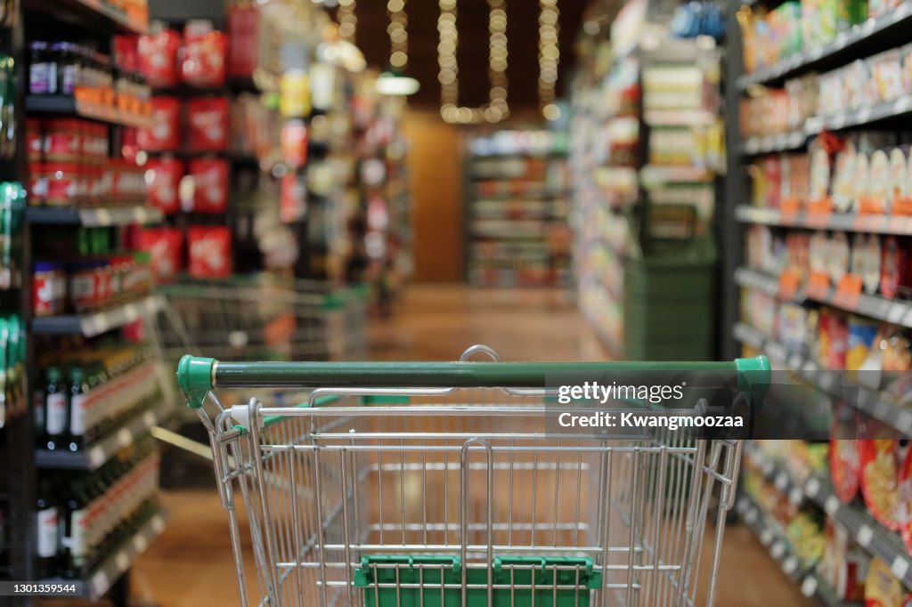Empty green shopping cart in supermarket aisle interior background