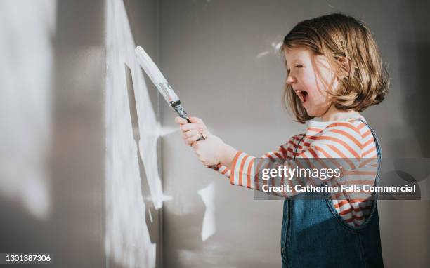 happy child painting a wall with white paint - happy dirty child stockfoto's en -beelden