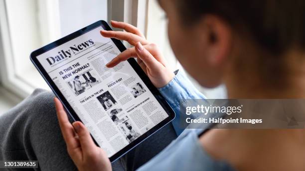 young woman indoors at home, reading news on tablet. - window display stock-fotos und bilder