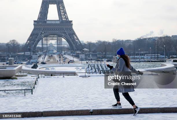 Woman wearing a protective face mask walks in the gardens of Trocadero covered in snow near the Eiffel Tower following a light overnight snowfall on...