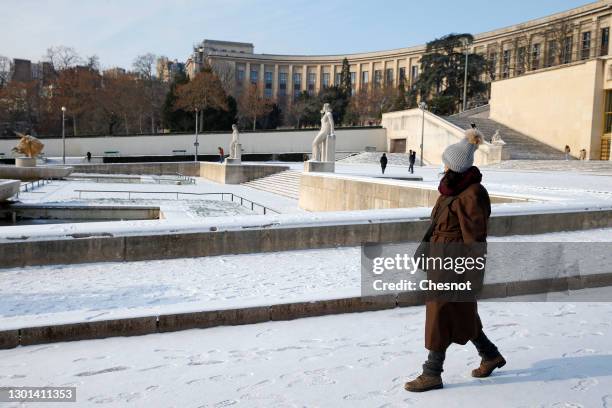 Woman wearing a protective face mask walks in the gardens of Trocadero covered in snow near the Eiffel Tower following a light overnight snowfall on...