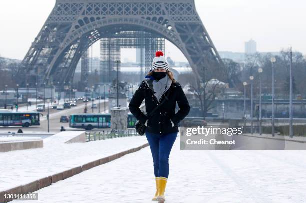 Woman wearing a protective face mask walks in the gardens of Trocadero covered in snow near the Eiffel Tower following a light overnight snowfall on...