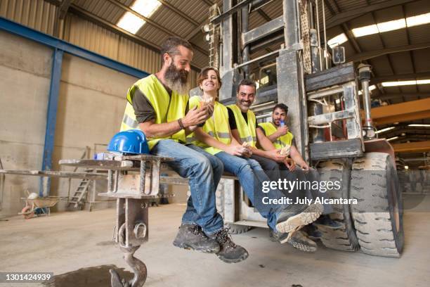 les ouvriers de construction prennent une pause grignotant sur les lames d’un chariot élévateur géant - bulle protection photos et images de collection