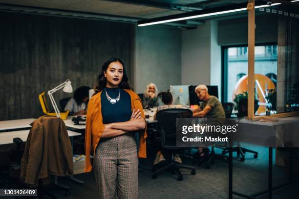 confident businesswoman with arms crossed while colleagues sitting in background at office - young business woman bildbanksfoton och bilder