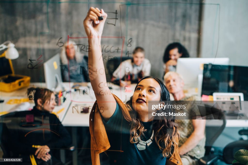 Businesswoman explaining strategy to colleagues while writing on glass at IT company