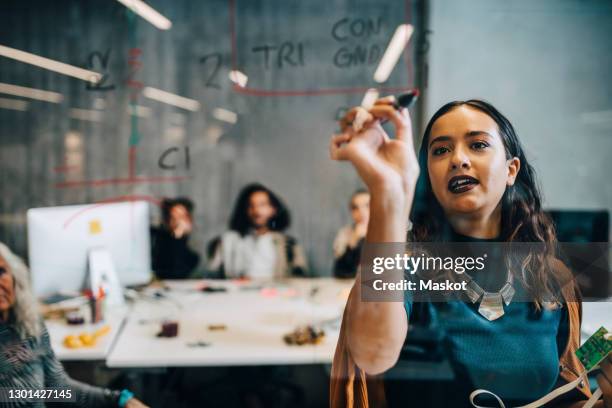 young businesswoman writing on glass while explaining strategy to colleagues in start up company - computer programmer ストックフォトと画像