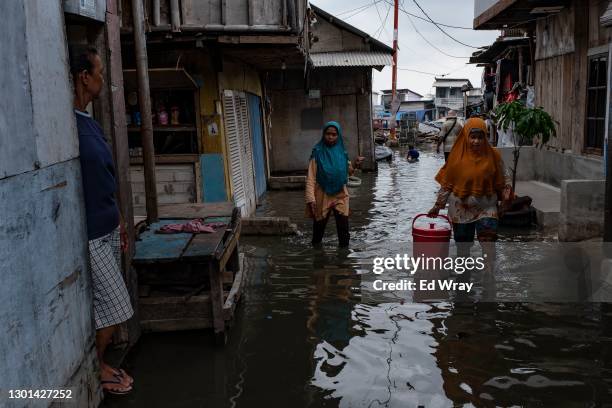 Indonesian women walk through a village which is flooded every morning with the high tide due to the sinking of coastal land on February 10, 2021 in...