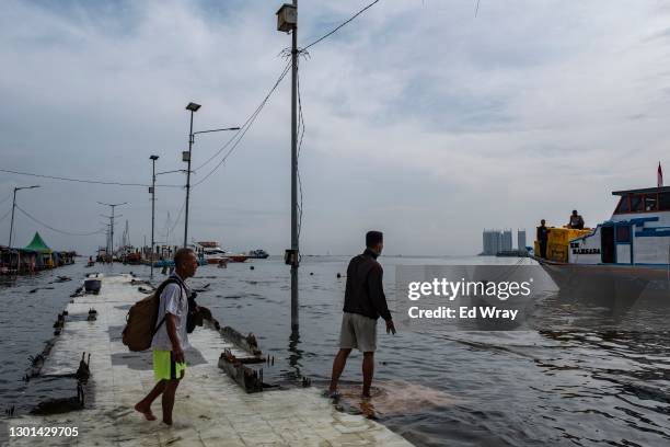 Indonesian men wait to board a ferry from the submerged walkway of a ferry terminal on the North coast of Jakarta which is flooded every morning...