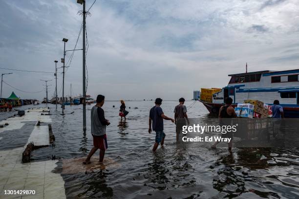 Indonesian men bring a load of produce to a ferry along the submerged walkway of a ferry terminal on the North coast of Jakarta which is flooded...