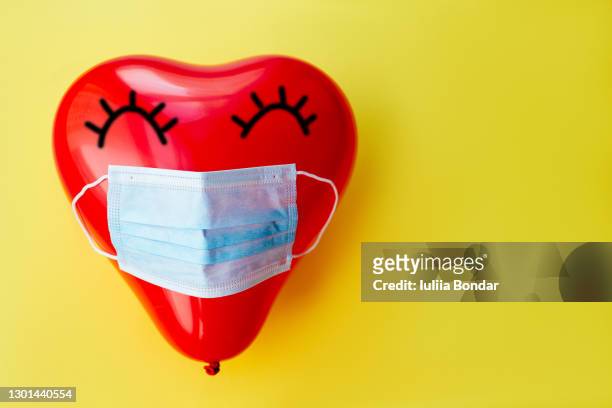 red heart baloon in medical mask on yellow background - funny surgical masks stock pictures, royalty-free photos & images