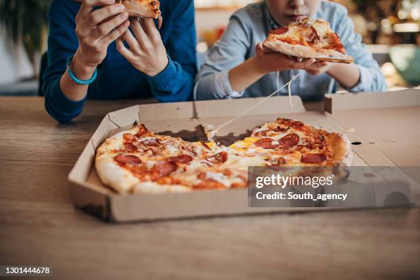 zwei brüder essen gemeinsam pizza - child delivering stock-fotos und bilder