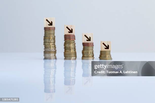 arrows on wooden blocks on top of descending stacks of coins against gray background. - recession stock pictures, royalty-free photos & images