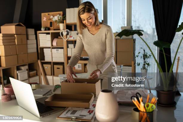 glimlachende jonge vrouw die de online orde van de klant in haar bureau verpakt - market trader stockfoto's en -beelden