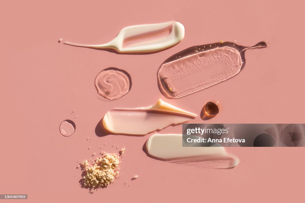 Drops and smears of various cosmetic products on pink background. Trendy selfcare products of the year