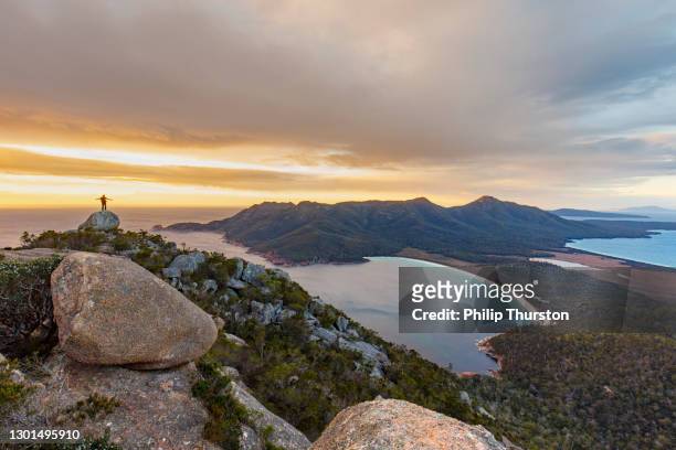 hiker on top of mountain at sunrise, wineglass bay tasmania - top of the mountain australia stock pictures, royalty-free photos & images