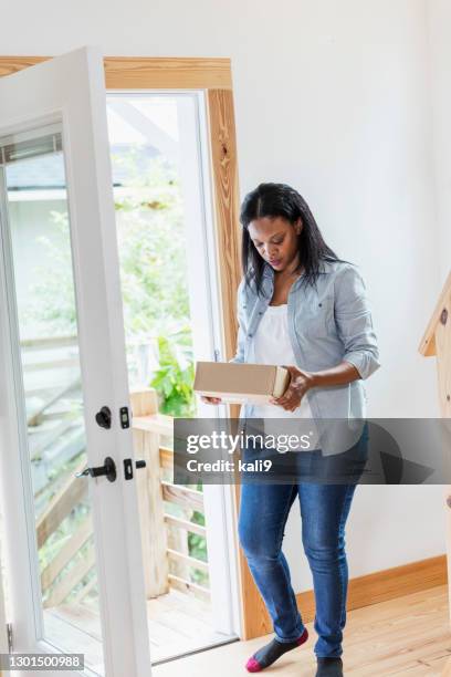 mujer negra en el interior, sosteniendo un paquete entregado a casa - umbral fotografías e imágenes de stock