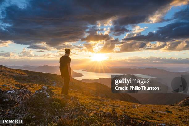man standing on cliff watching sunset over golden mountain range - extreme terrain stock pictures, royalty-free photos & images