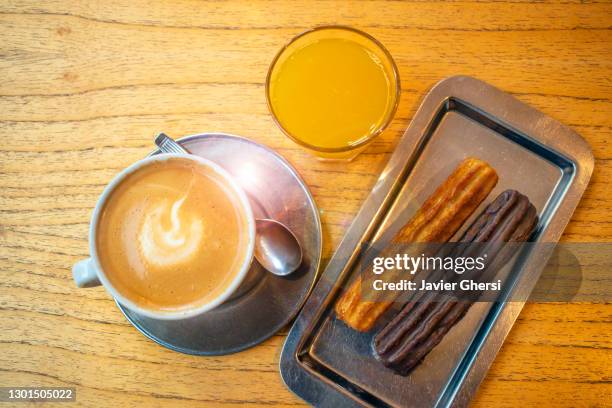 café con leche con churros rellenos de dulce de leche (uno bañado en chocolate) y jugo de naranja exprimido. - chocolate con churros stock pictures, royalty-free photos & images