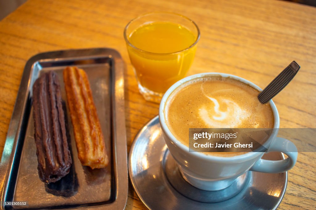 Café con leche con churros rellenos de dulce de leche (uno bañado en chocolate) y jugo de naranja exprimido.
