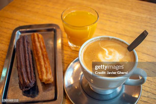 café con leche con churros rellenos de dulce de leche (uno bañado en chocolate) y jugo de naranja exprimido. - chocolate con churros stock pictures, royalty-free photos & images