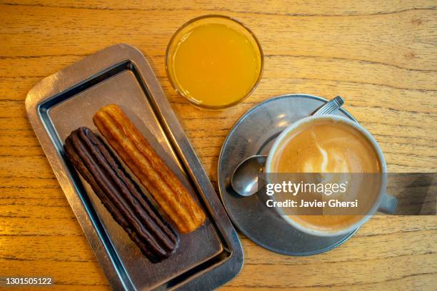 café con leche con churros rellenos de dulce de leche (uno bañado en chocolate) y jugo de naranja exprimido. - chocolate con churros stock pictures, royalty-free photos & images