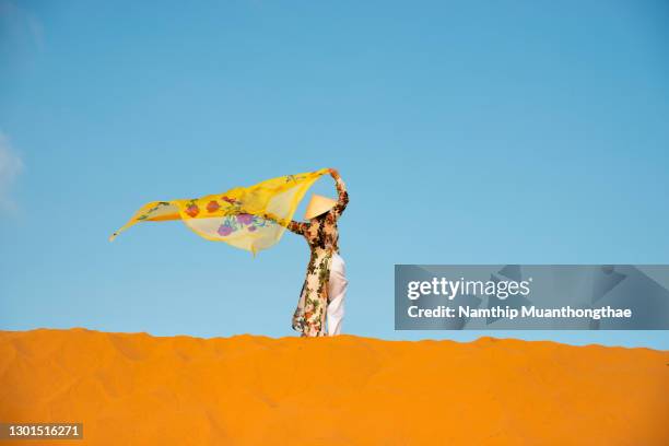 a vietnam woman on the top of desert with the traditional vietnamese clothes under the sunlight of blue sky shows a beautiful scenery of traditional ao dai clothes. - ao dai stockfoto's en -beelden